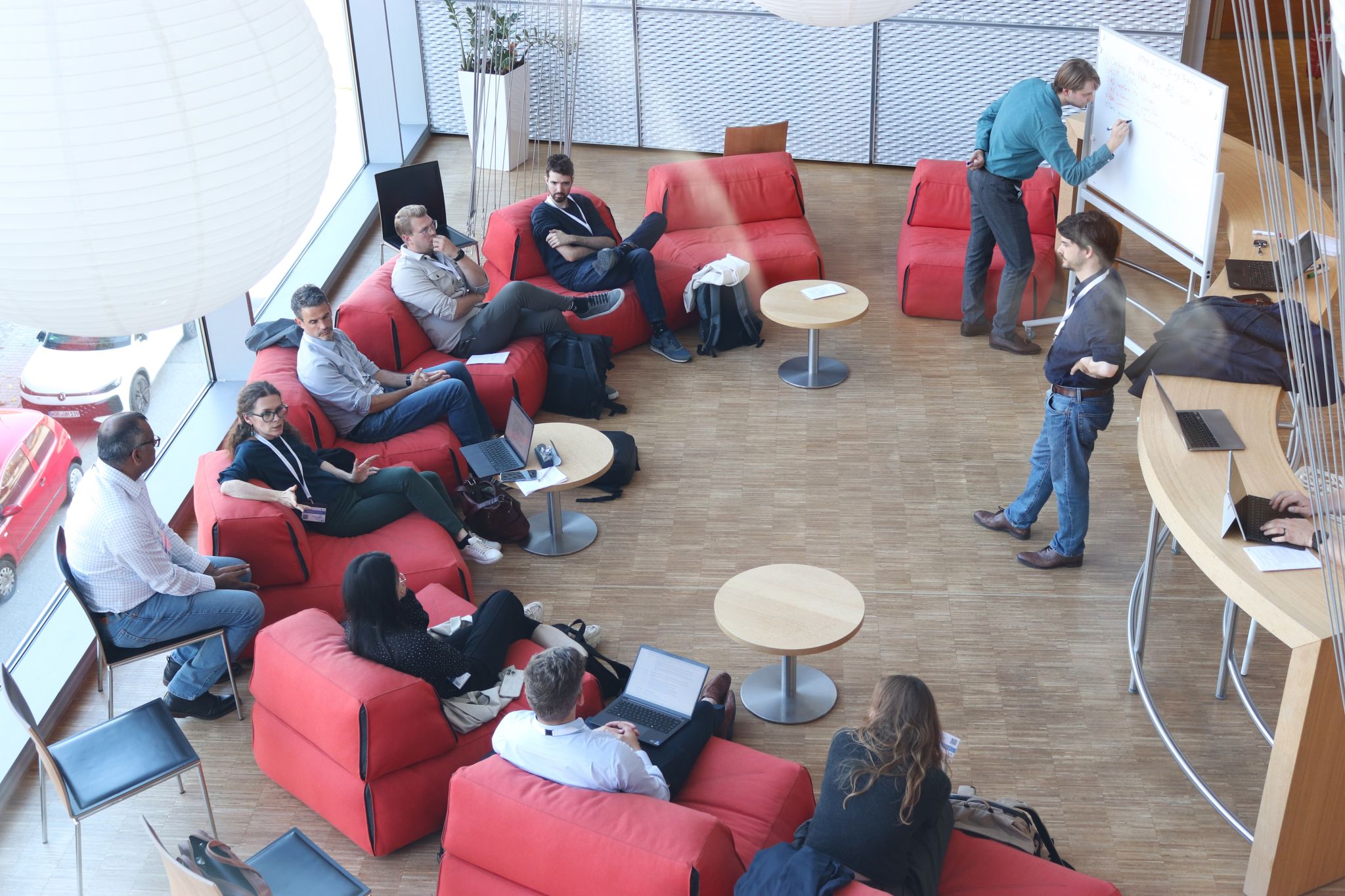 Workshop participants seated on red sofas around a whiteboard during a working-group discussion